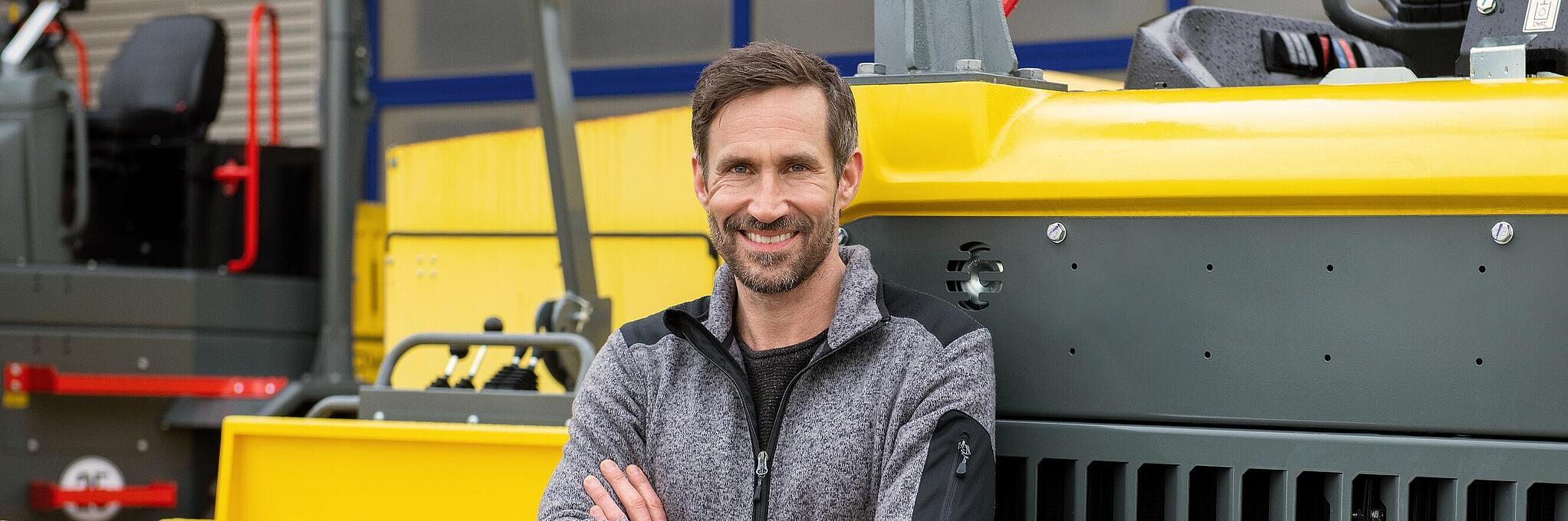 Smiling Wacker Neuson employee, arms crossed, leaning against a Wacker Neuson construction machine.