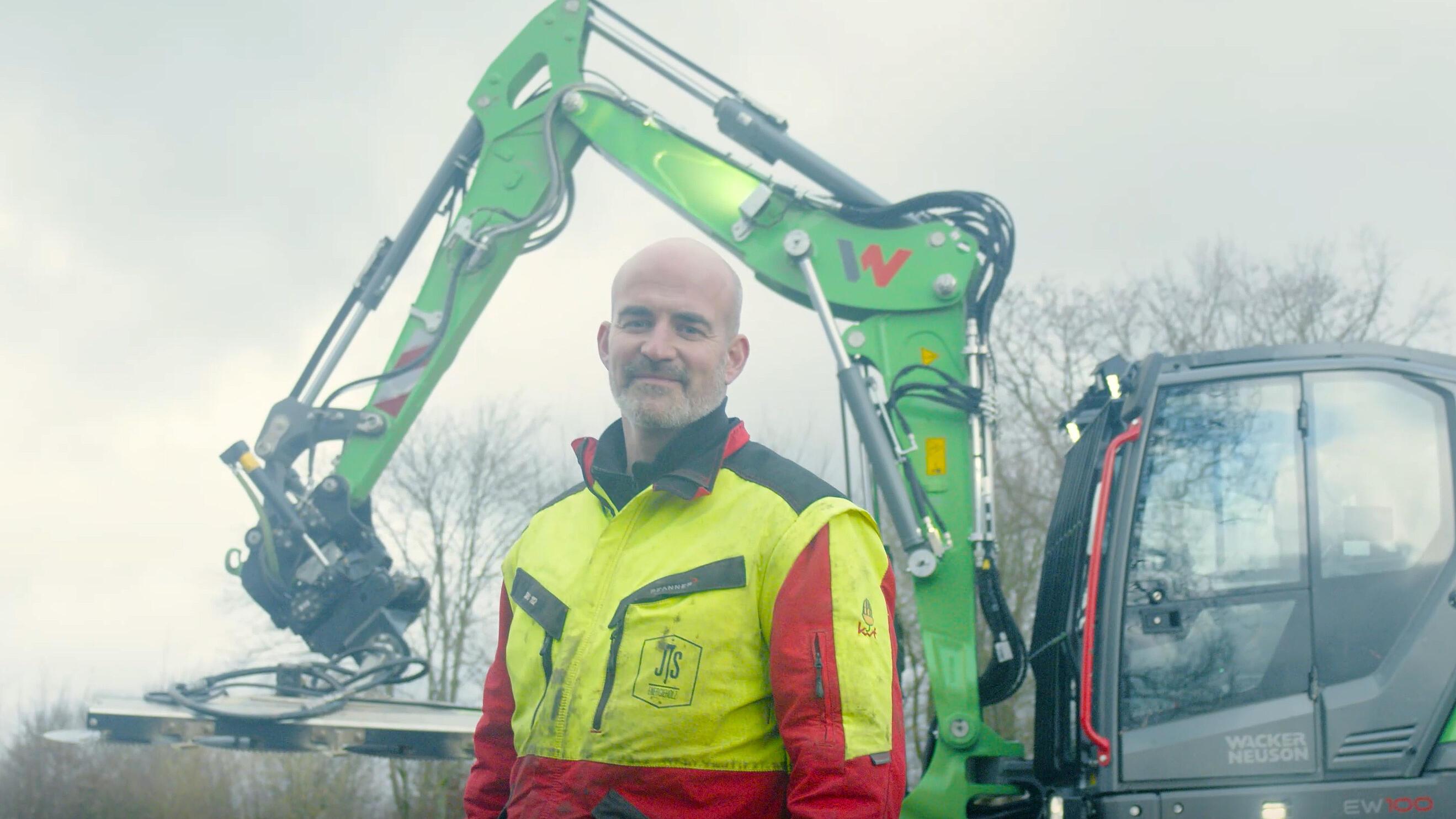 Een machinist staat voor een Wacker Neuson EW100-graafmachine op wielen, uitgerust met een tiltrotator.