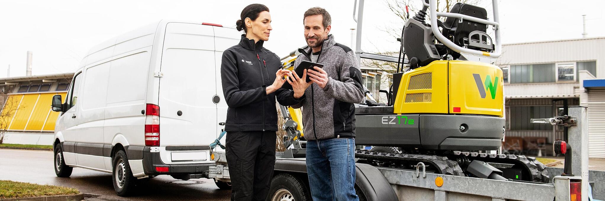 Des articles de merchandising Wacker Neuson sont posés sur une table au premier plan, collaborateur Wacker Neuson en arrière-plan.