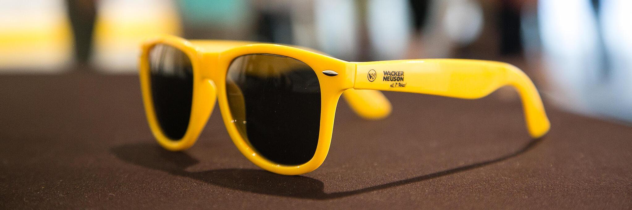 Gelbe Sonnenbrille mit Wacker Neuson Logo.