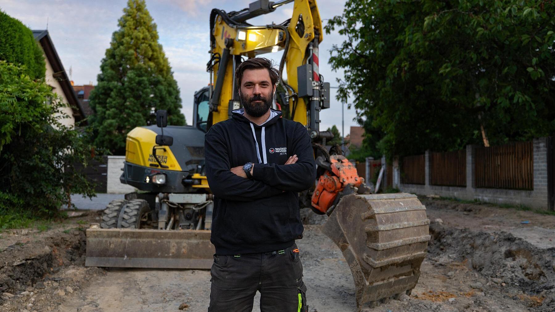 Een bouwvakker staat op een bouwplaats voor een Wacker Neuson EW100-graafmachine op wielen.